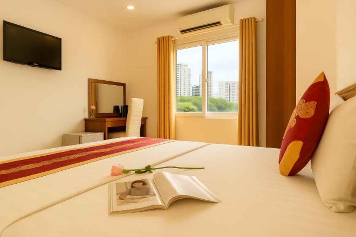 Camera d'albergo con un letto grande, una televisione a schermo piatto montata a parete, una scrivania con una sedia e una finestra con tende.