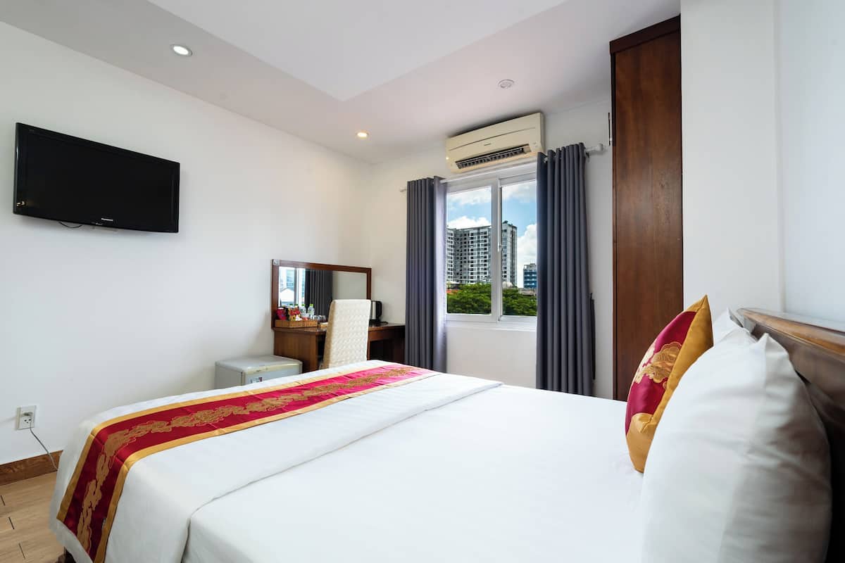 Une chambre d’hôtel avec un lit, un bureau, une chaise, une télévision et une fenêtre avec des rideaux.