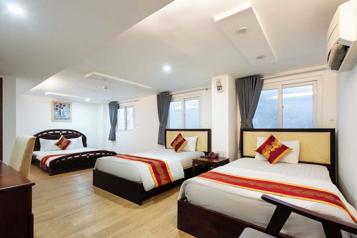 Une chambre d’hôtel avec trois lits, un plancher en bois et une grande fenêtre.