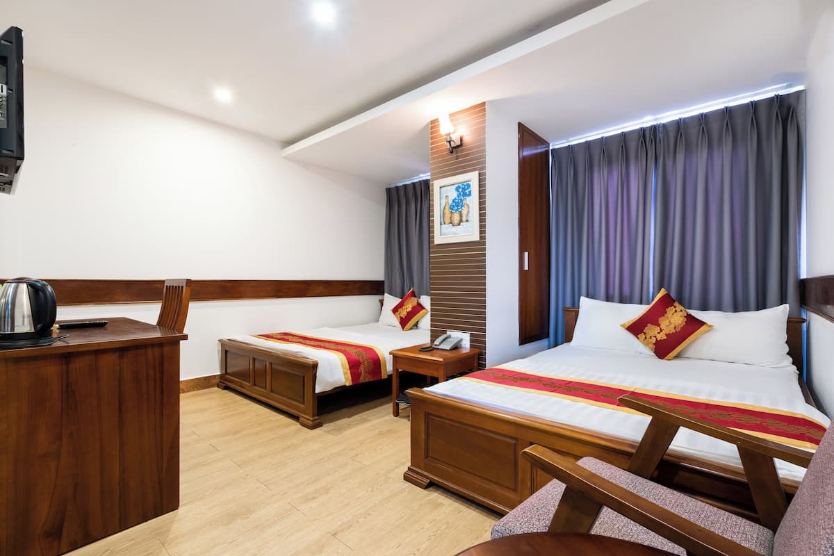 Une chambre d’hôtel avec deux lits, un bureau en bois, un téléphone et un tableau au mur.