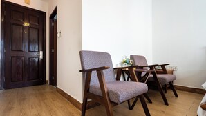 Une pièce avec un plancher en bois, deux fauteuils rembourrés à ossature en bois, une petite table et une porte en bois foncé.