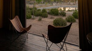 A room with a large glass door leading to an outdoor area with chairs and a view of a landscape with trees and a body of water. - Mineral del Cielo (Pozos)
