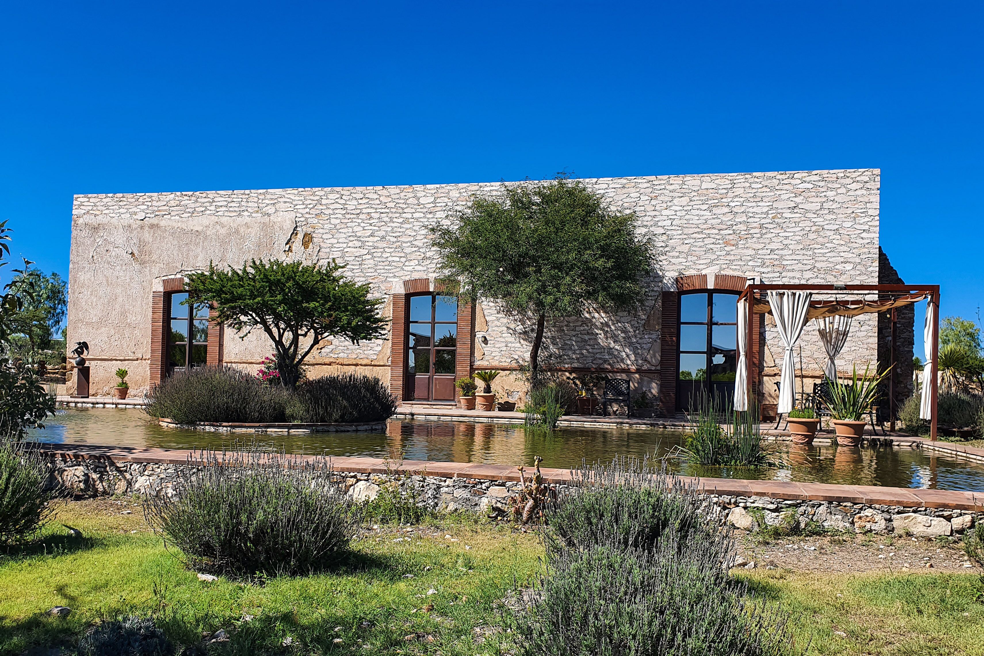 A stone building with large windows, a garden with a pond, and outdoor furniture.