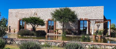 A stone building with large windows, a garden with a pond, and outdoor furniture.