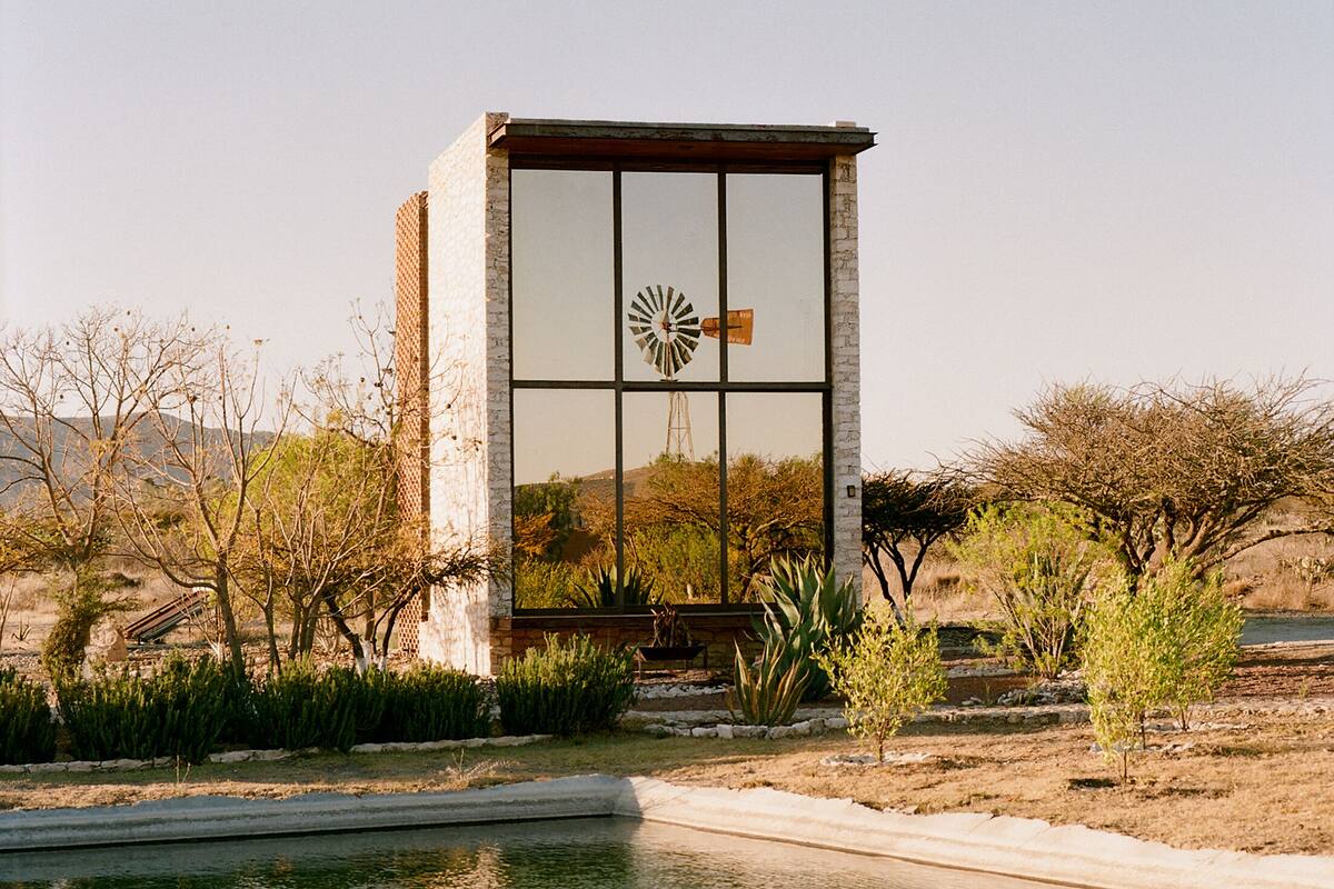A modern building with a large window and a windmill symbol, surrounded by a landscaped garden and a body of water.
