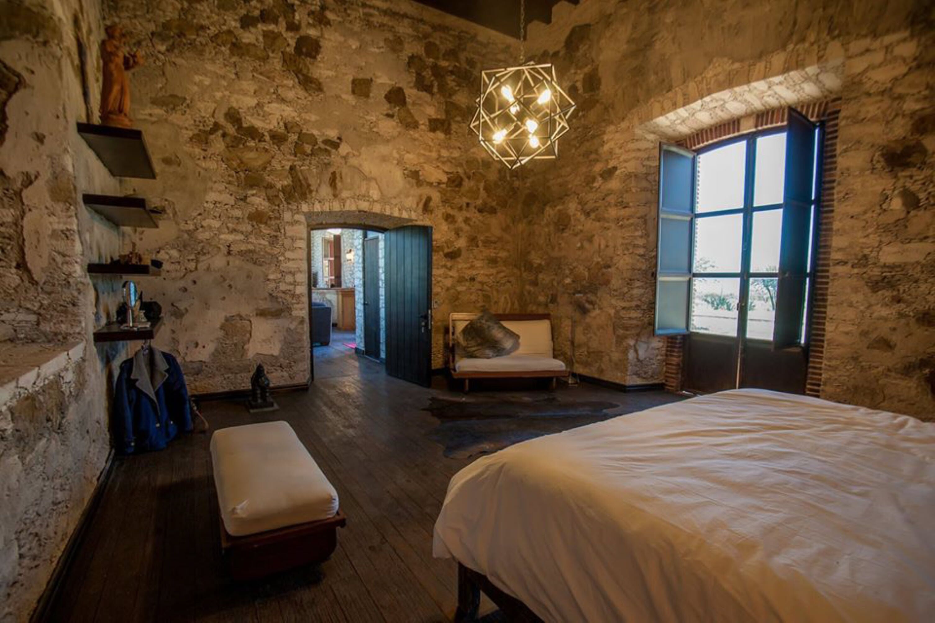 A rustic room with exposed brick walls, a large bed, a bench, and a hanging light fixture.
