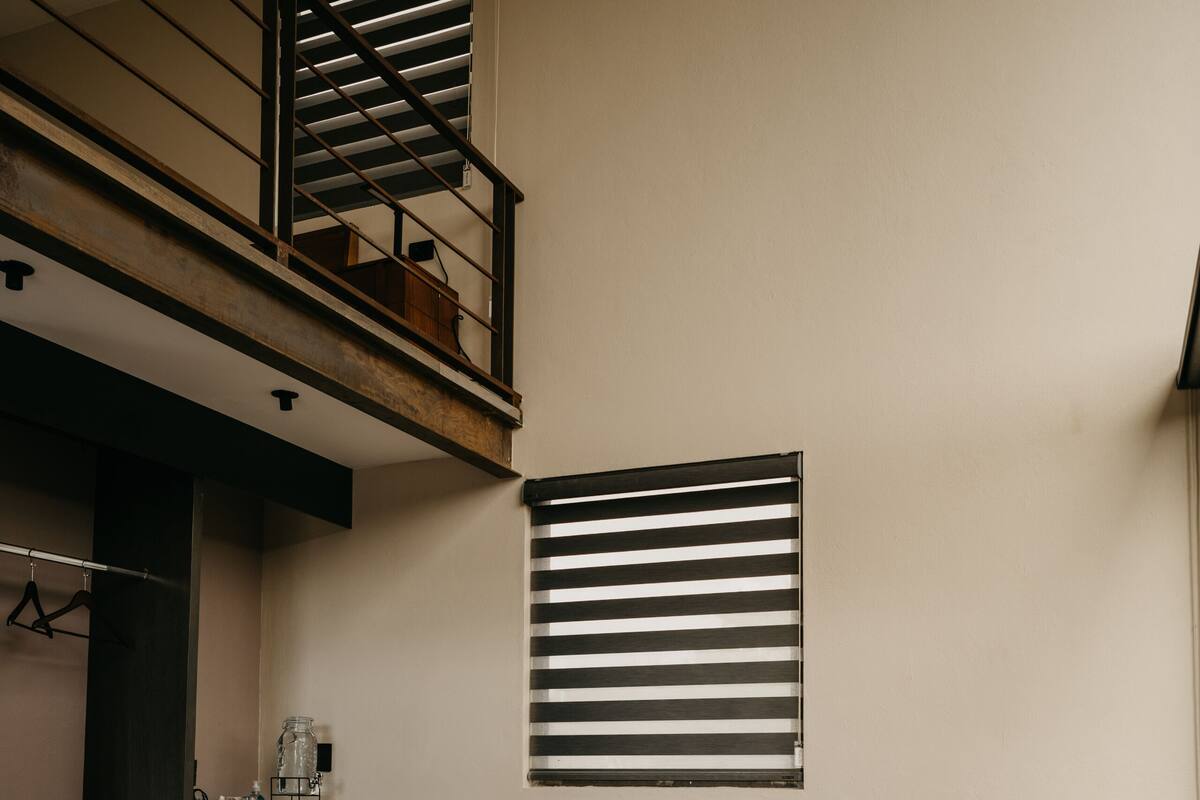 A modern living room with a sofa, a glass coffee table, a striped rug, a dark wooden cabinet, and a staircase with a railing.