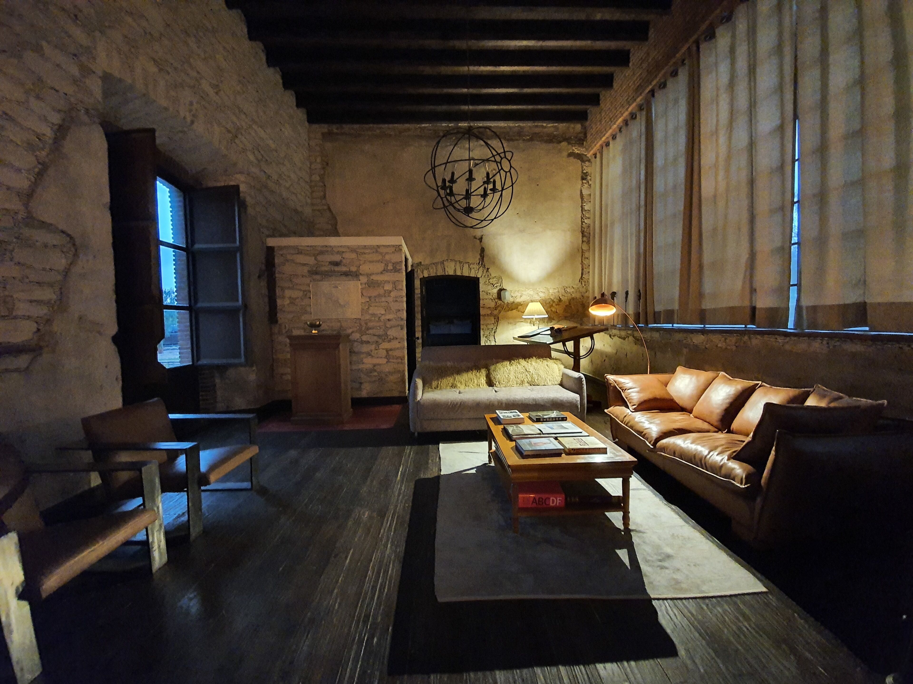 Una sala de estar acogedora con pared de piedra, un sofá de cuero, una mesa de centro de madera con libros, una lámpara y un televisor sobre un mueble.