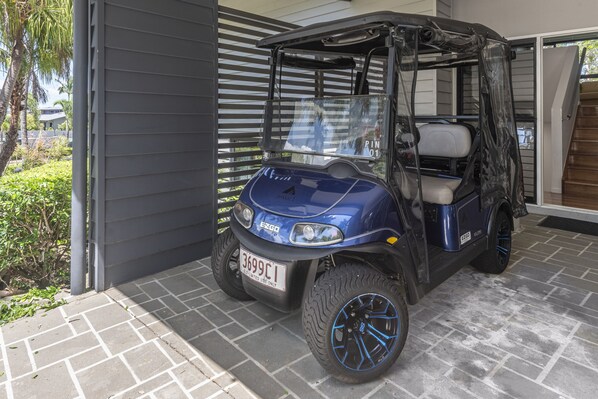A blue utility vehicle parked in a covered area with a garage door and a staircase leading to a second floor.