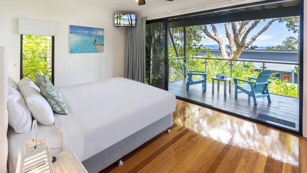 Un dormitorio con una cama grande, una mesita de noche, vistas al exterior y un balcón con sillas.