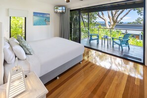 Ein Schlafzimmer mit einem großen Bett, einem Nachttisch, Blick ins Freie und einem Balkon mit Sitzgelegenheiten.