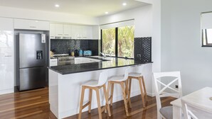 Una cocina moderna con un refrigerador de acero inoxidable, una encimera negra y taburetes de bar de madera.