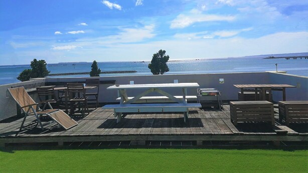 Une terrasse sur le toit, aménagée avec des meubles en bois, une table blanche et offrant une vue sur la mer et une jetée.