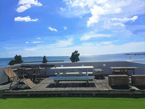 Une terrasse sur le toit, aménagée avec des meubles en bois, une table blanche et offrant une vue sur la mer et une jetée.