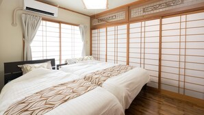 Une chambre de style japonais traditionnel, dotée d’un grand lit, de portes coulissantes de type « shoji » et d’un appareil de climatisation.