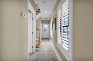 A hallway with a tiled floor, a white door, and a window with blinds.