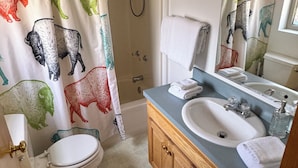 Een badkamer met douchegordijn met dierenprint, een toilet, een wastafel met spiegel en houten kastjes.
