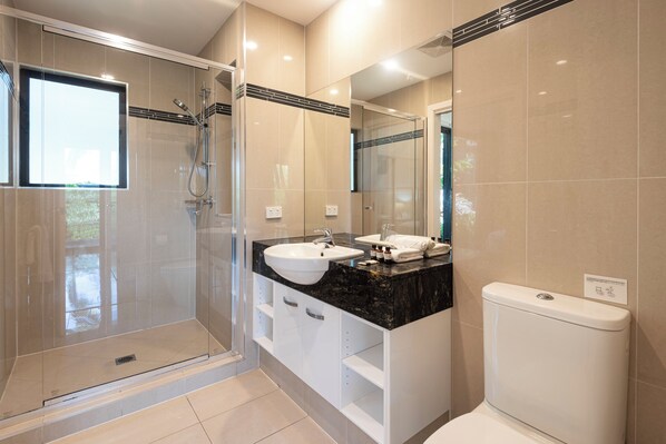 Un baño moderno con ducha de vidrio, lavamanos blanco y retrete.