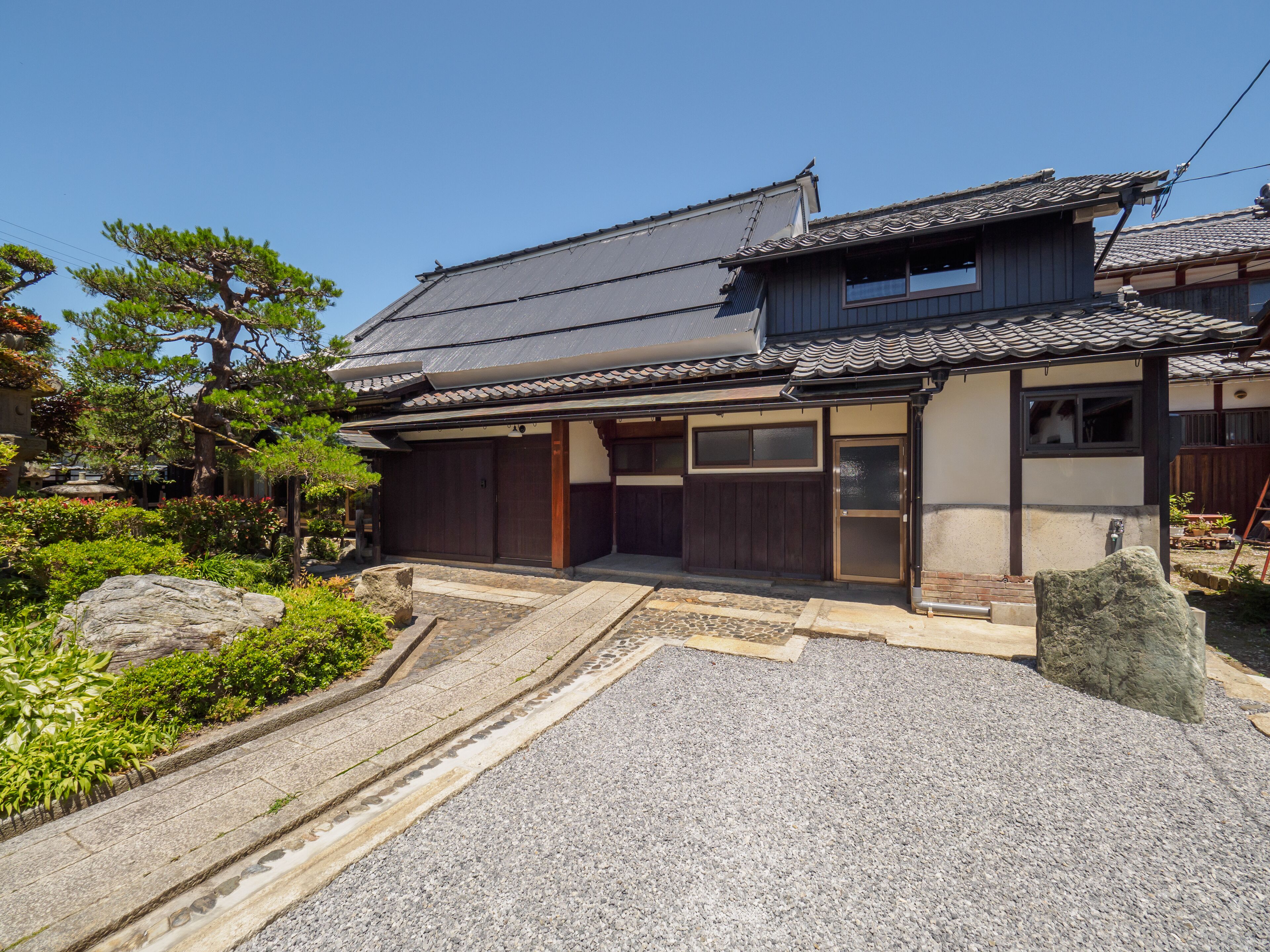 A traditional Japanese house with a tiled roof, wooden doors, and a stone pathway leading to the entrance.