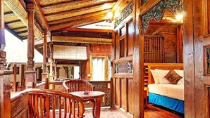 A wooden cabin interior with a bed, a dining table with chairs, and a balcony.