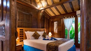 A wooden room with a bed, a nightstand, and a window with curtains.
