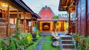 A traditional wooden house with a red tiled roof, a central courtyard with a stone pathway, and a small boat on the steps.