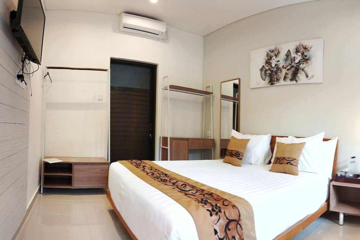Ein Hotelzimmer mit einem großen Bett, einem Nachttisch mit Lampe, einem Fenster mit Vorhängen und einer Wand-Klimaanlage.