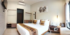 A hotel room with a large bed, a bedside table with a lamp, a window with curtains, and a wall-mounted air conditioner. - Villa & Hotel B52 Gili Air (Gili Air)