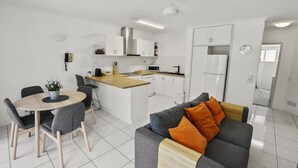 Une cuisine moderne avec des meubles blancs, un îlot central et un coin repas comprenant une table ronde et des chaises.