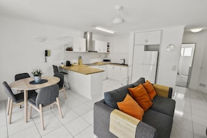 A modern kitchen with white cabinets, a central island, and a dining area with a round table and chairs.