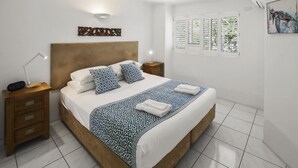 Une chambre bien rangée, avec un lit, des tables de chevet, une œuvre d’art accrochée au mur et une fenêtre équipée de stores.
