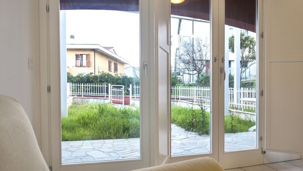 A room with a sliding glass door leading to an outdoor area with a white fence and greenery. - S010 - Sirolo, new three-room apartment with garden (Sirolo)