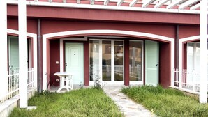 A building with a red facade, white trim, and a covered porch with a table and chairs. - S010 - Sirolo, new three-room apartment with garden (Sirolo)