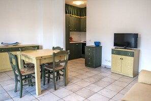 A compact living space with a dining table, chairs, a TV, and a kitchenette.