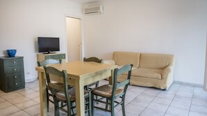 A dining area with a table and chairs, a television on a stand, a sofa, and a cabinet. - S010 - Sirolo, new three-room apartment with garden (Sirolo)