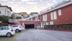 A building with a red facade, a covered staircase, and a parking area with two cars. - S010 - Sirolo, new three-room apartment with garden (Sirolo)
