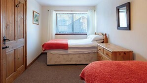 Un dormitorio con cama, cómoda de madera, ventana con cortinas, lámpara colgante y puerta con perchero.