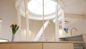 Una cucina moderna con una finestra a soffitto, una scala bianca e un vaso con fiori sul bancone.