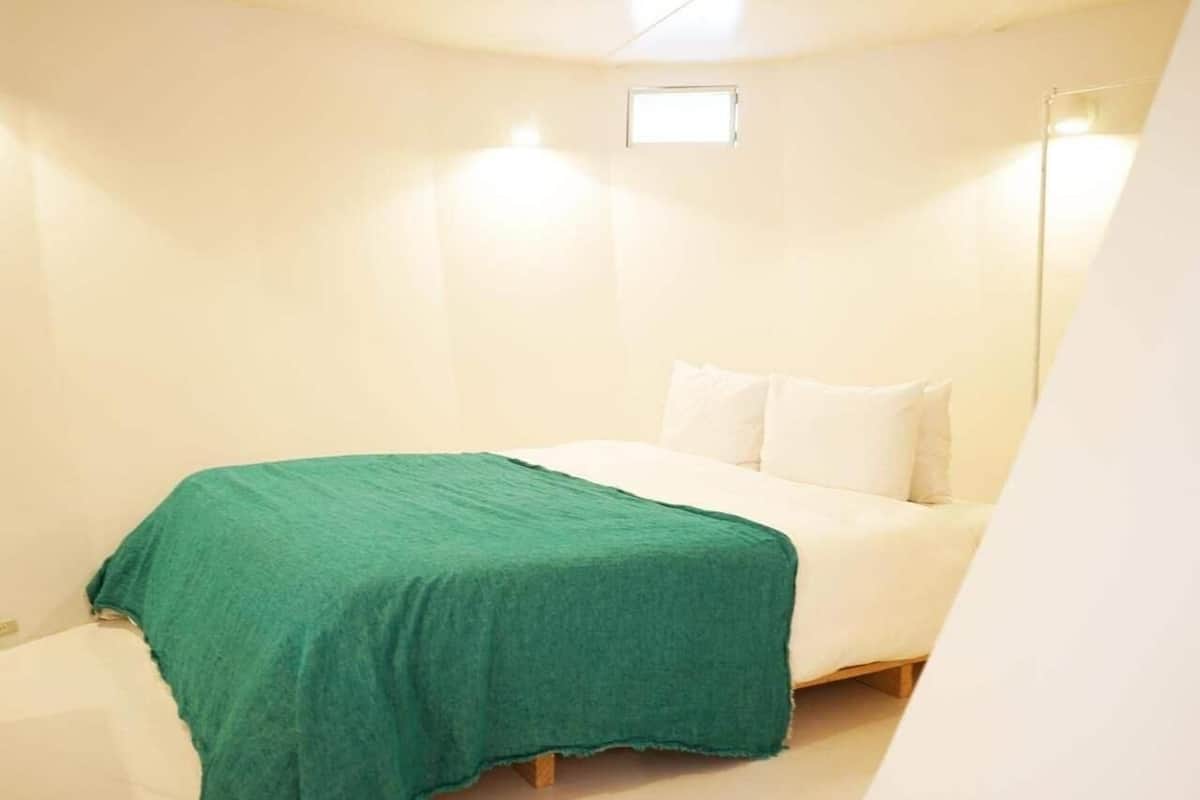 A small, cozy bedroom with a single bed, a green blanket, and a white pillow.
