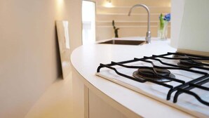 Una cucina moderna con un piano di lavoro bianco, un fornello a gas e un lavello in acciaio inossidabile.