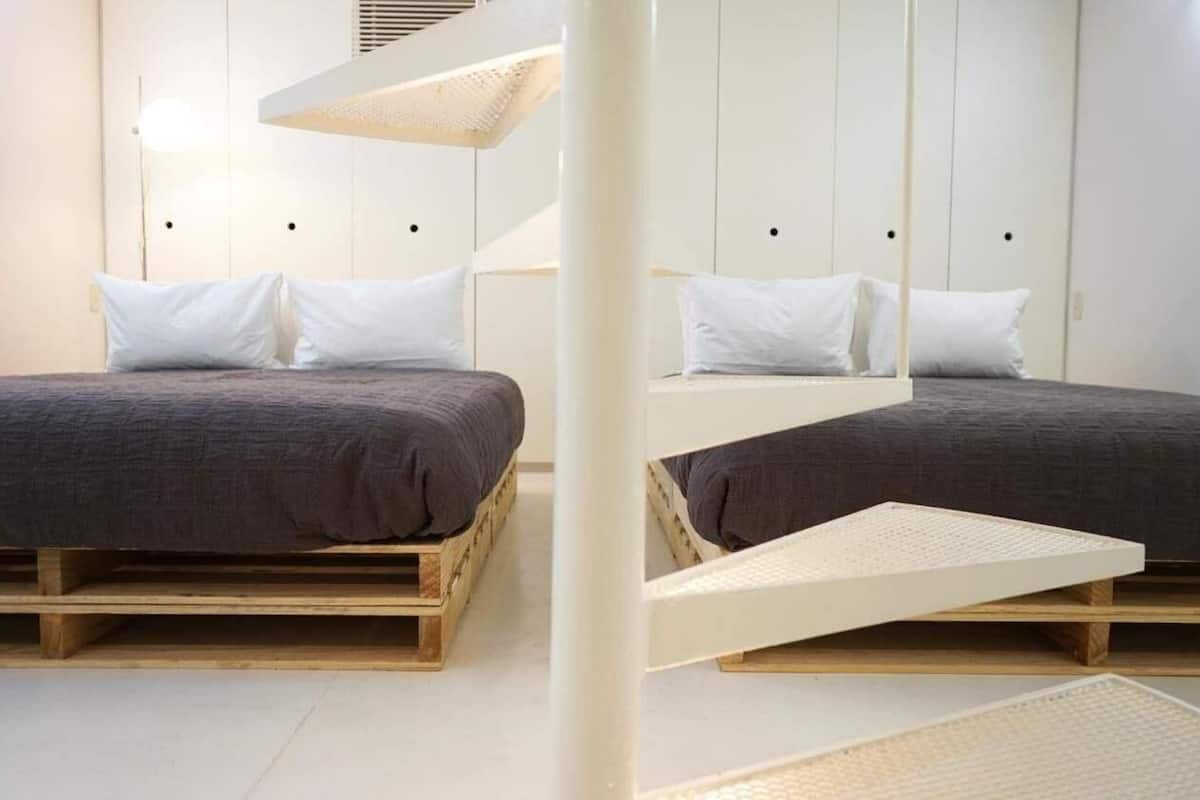 A modern bedroom with two wooden beds, white walls, and a unique ceiling design.