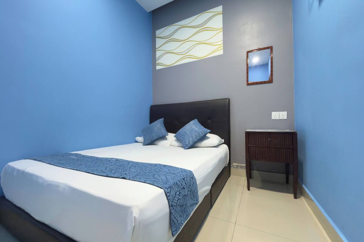 A bedroom with a bed, a nightstand, a wall-mounted mirror, and a decorative light fixture.