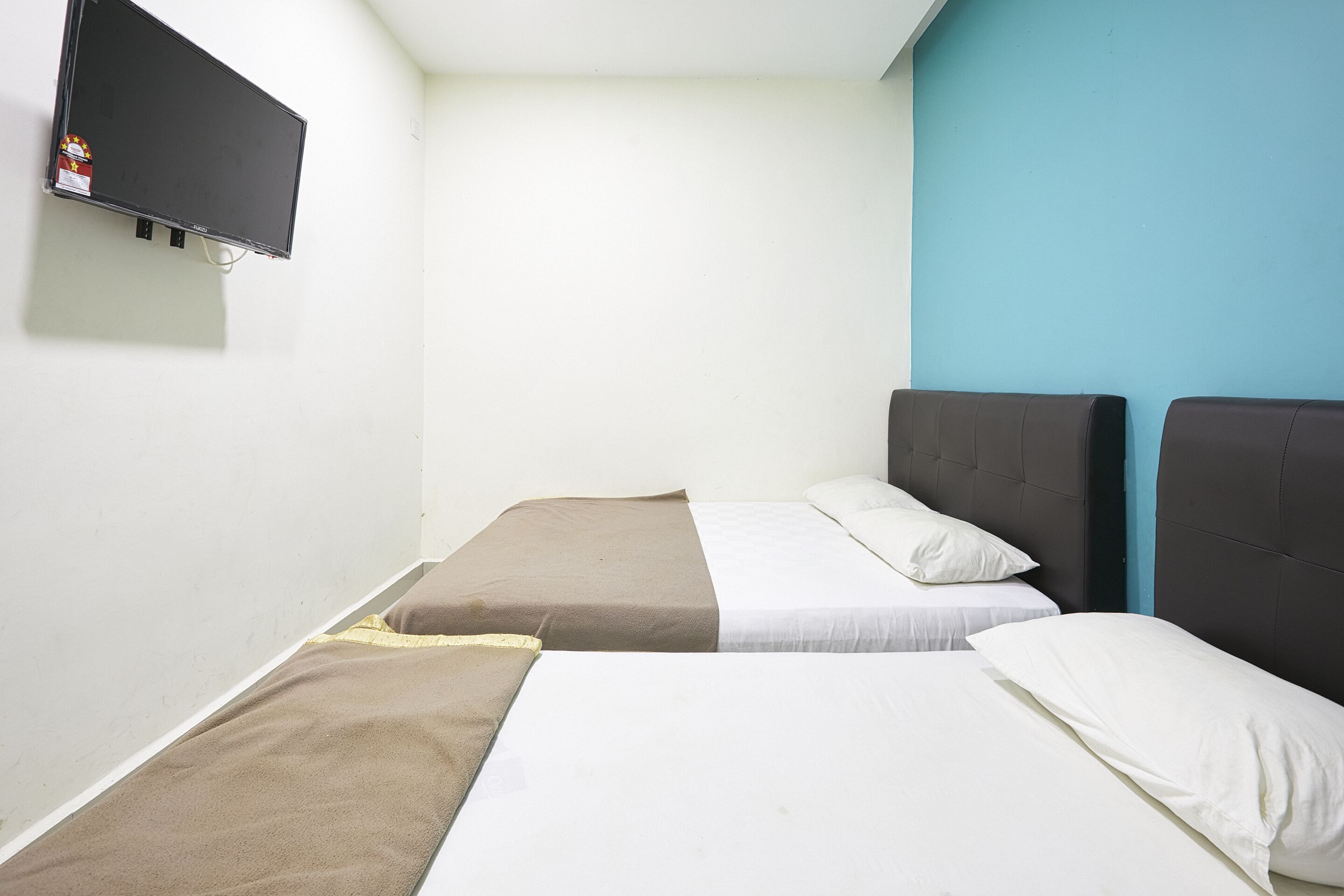 A small, simple room with two beds, a flat-screen TV, and a blue accent wall.