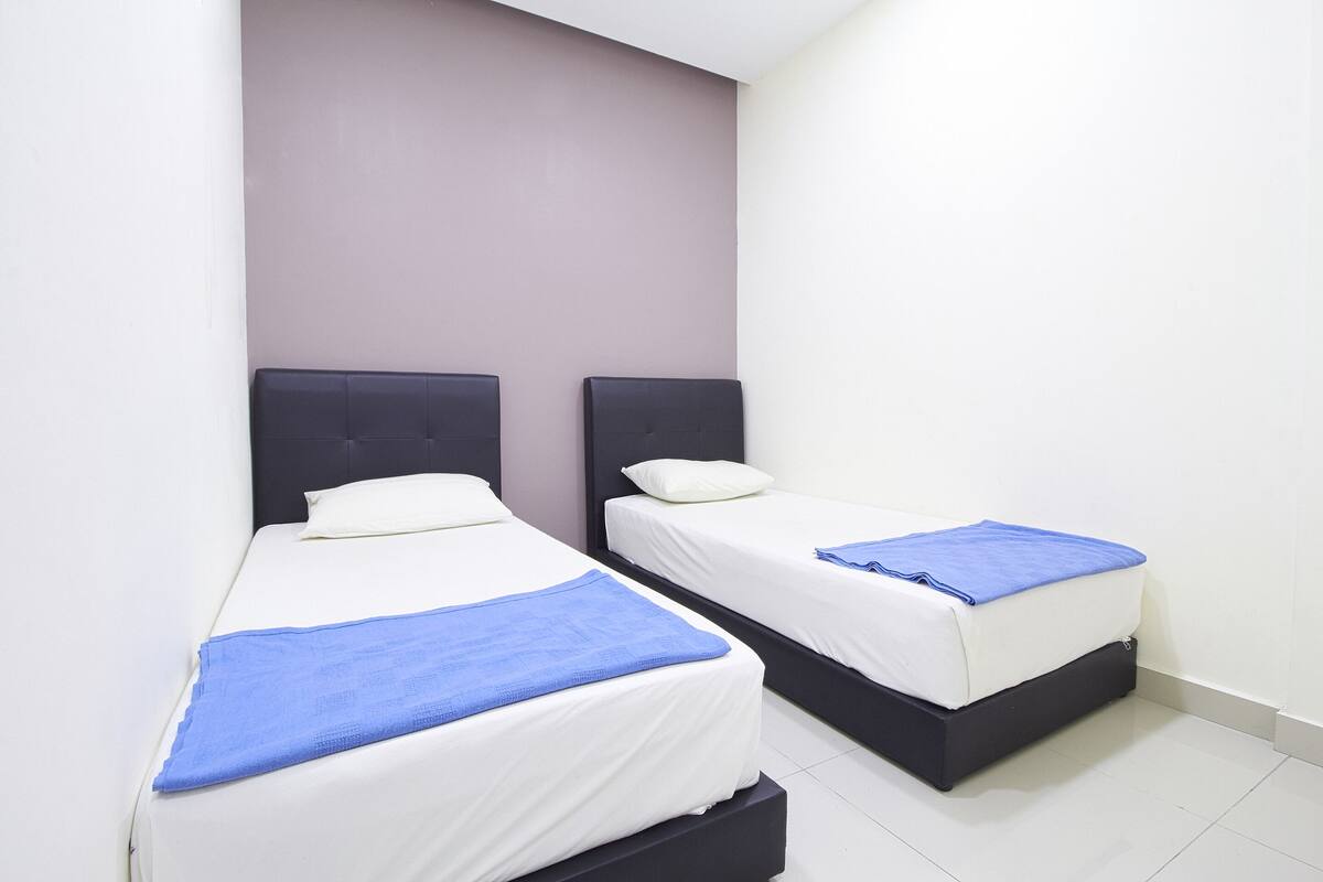Two single beds with black headboards, white bedding, and blue blankets in a room with white walls and a tiled floor.