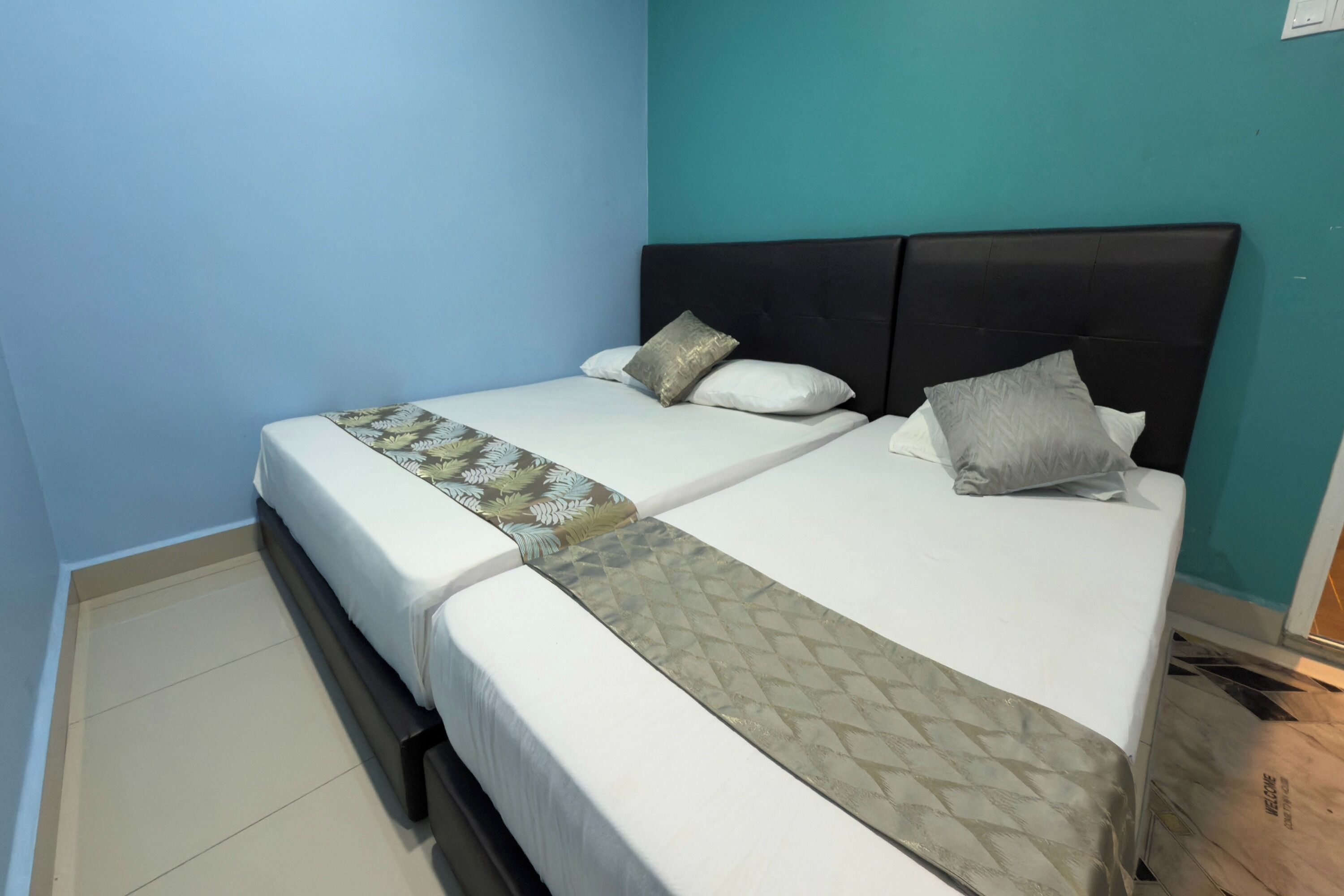 A double bed with a patterned bedspread and two pillows, a dark headboard, and teal walls.