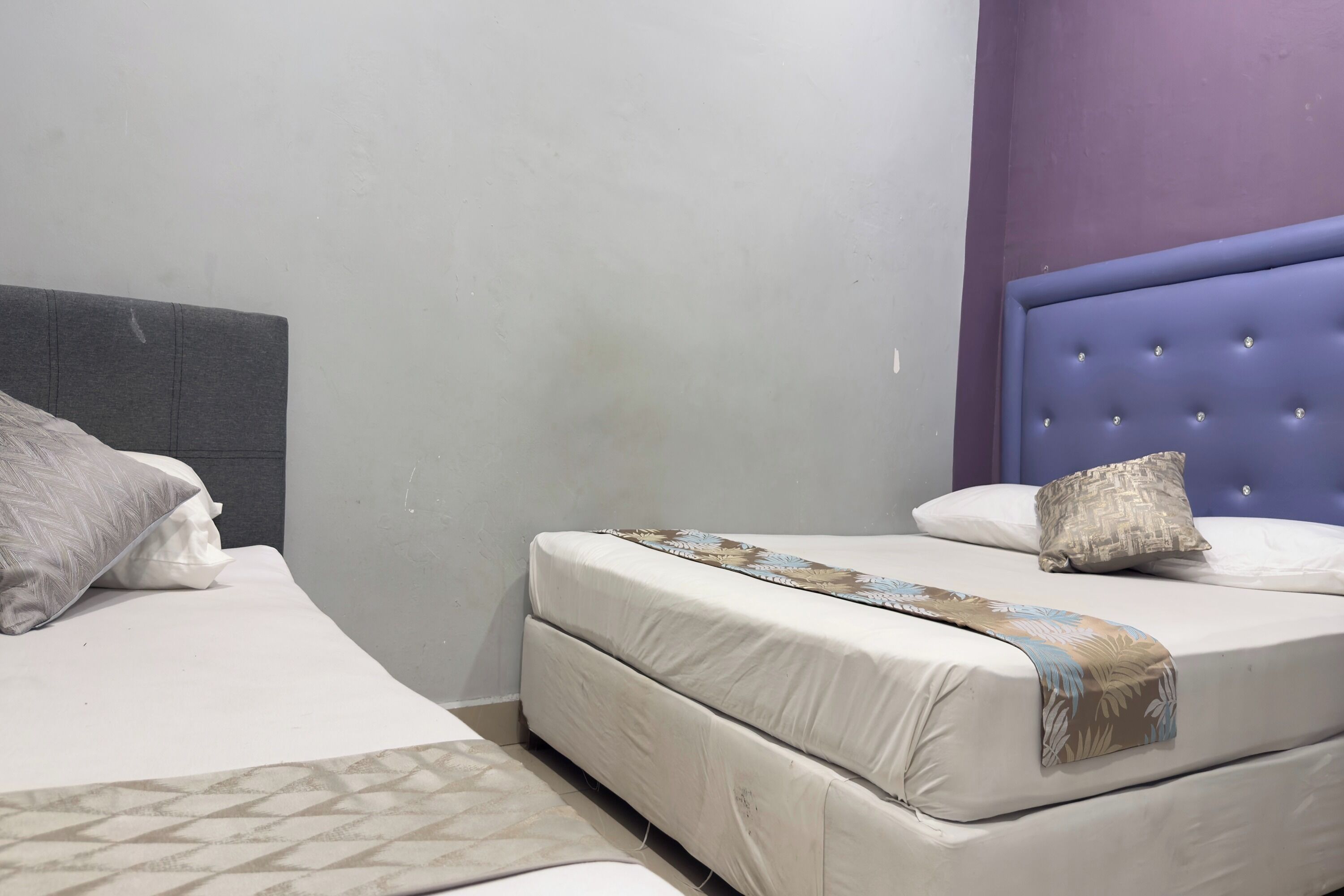 A bedroom with two beds, one with a grey headboard and the other with a purple headboard.