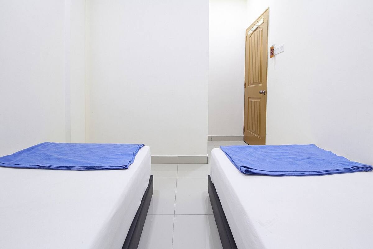 A room with two beds, each with a blue towel, white walls, a wooden door, and a white tiled floor.