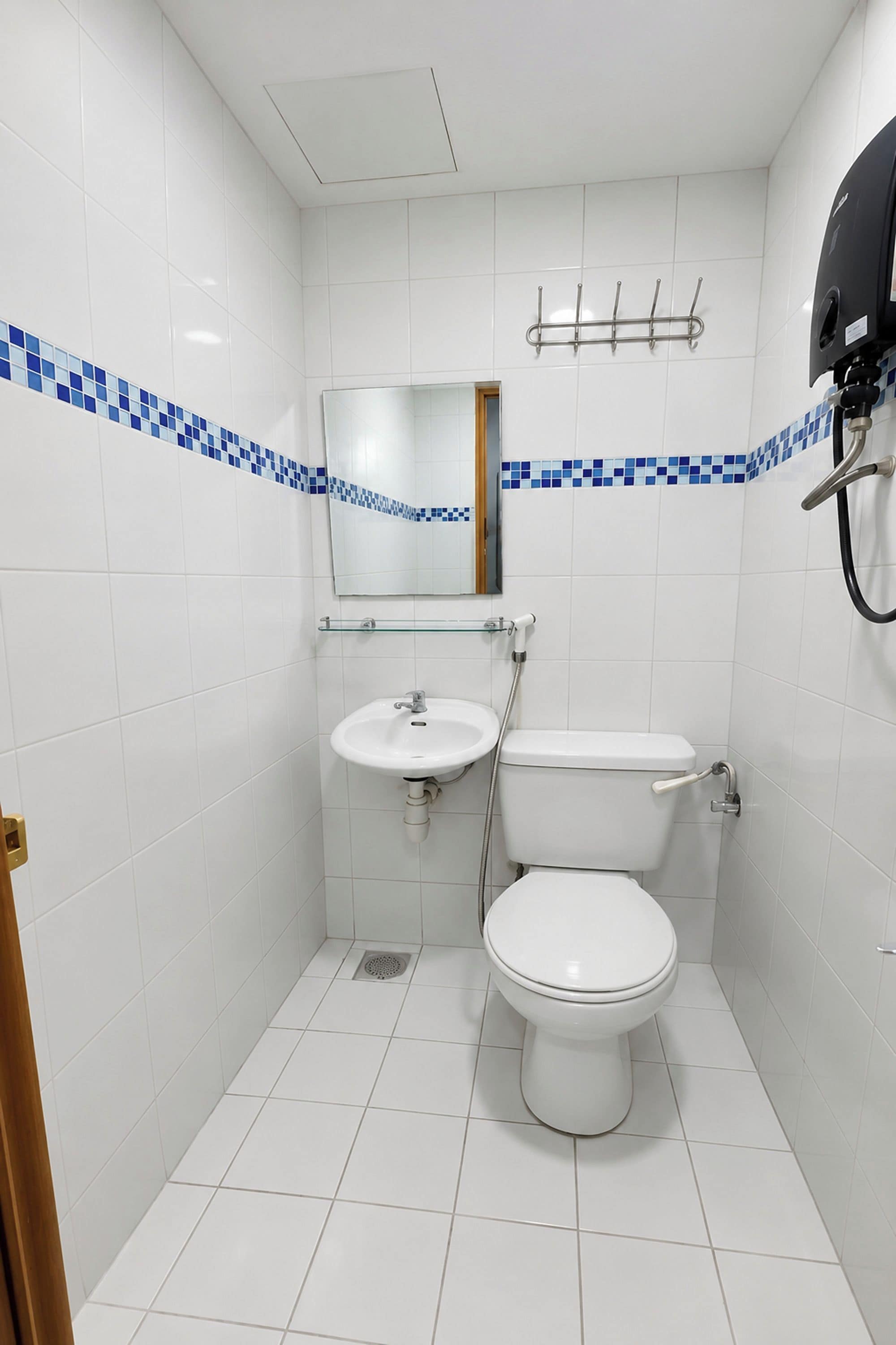 Un baño pequeño y limpio, con azulejos blancos, un lavamanos blanco, un inodoro y un espejo.