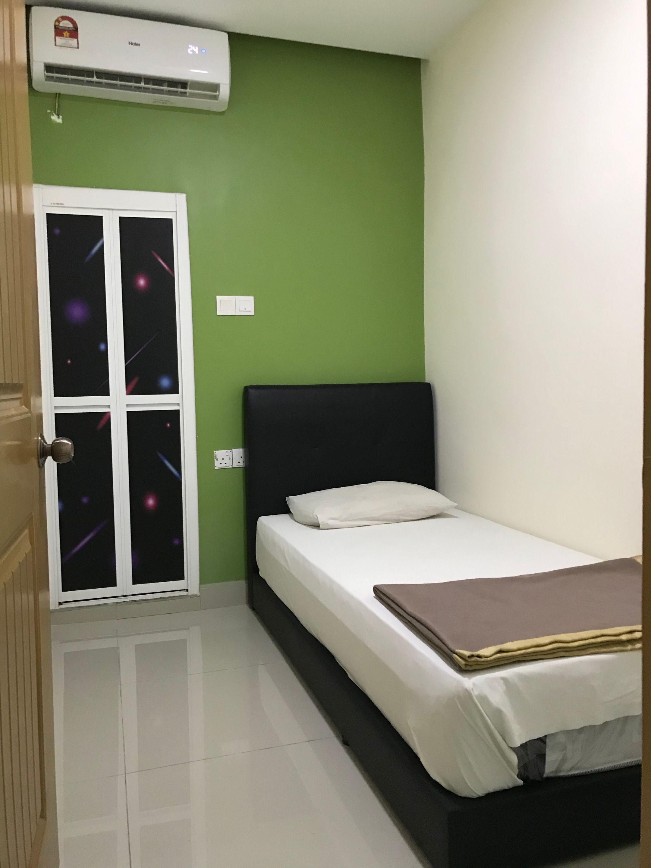 A bedroom with a bed, a nightstand, a window with a view of the sky, and an air conditioning unit.