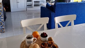 Un comedor con una mesa dispuesta para el desayuno, que incluye pan, fruta y bollería.